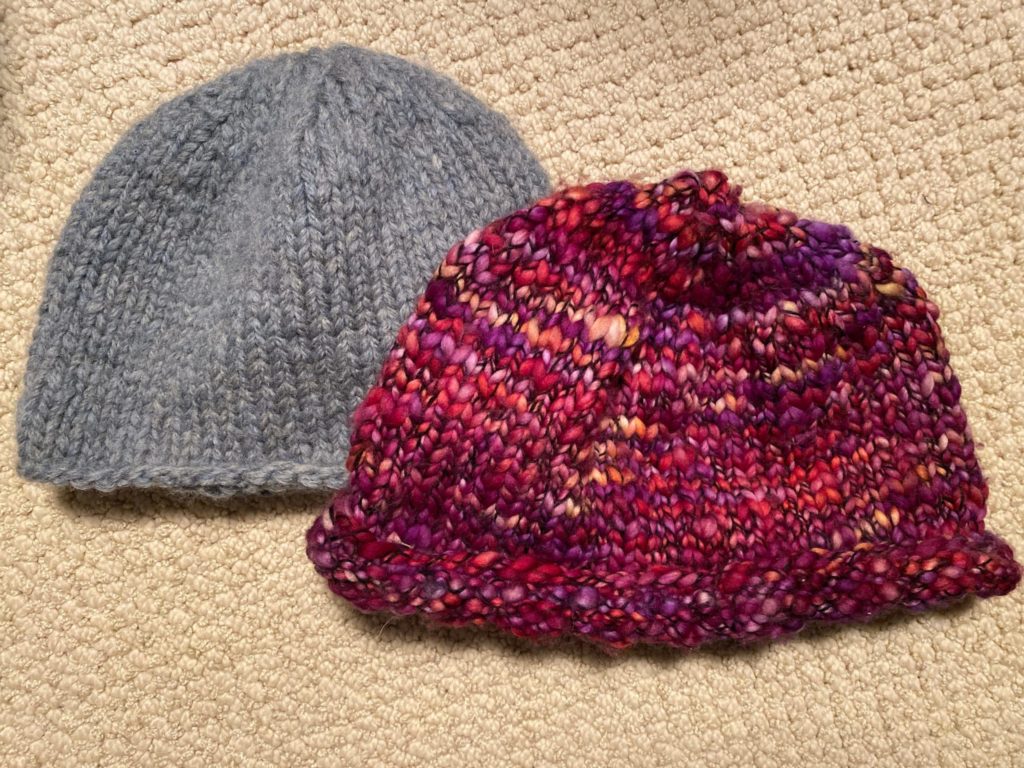 Two hats knitted by hope during the pandemic, grey on the left and pink on the right