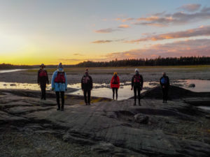 Six students stand facing the camera in front of a beautiful sunset