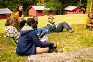 Students sit outside for their science class, with cabins in the background